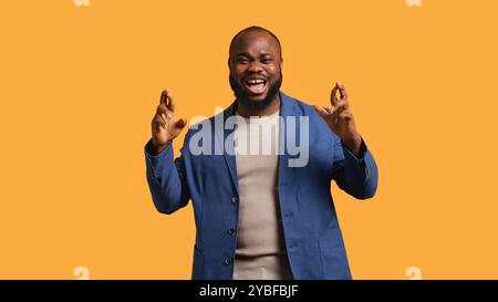 Portrait d'homme afro-américain optimiste croisant les doigts, faisant du vœu, isolé sur fond jaune de studio. Jolly BIPOC personne espérant bonne chance, attendant le miracle, caméra B. Banque D'Images