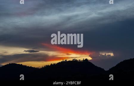 Chiang mai, Thaïlande. 18 octobre 2024. Les derniers rayons du soleil couchant disparaissent lentement au-dessus de l'horizon, avec le grand Bouddha debout en toile de fond à Wat Phra That Doi Kham. Les reflets du ciel au coucher du soleil affichent une variété de couleurs, telles que des teintes dorées et rouges, qui peuvent être vues chaque année en octobre avant l'arrivée de la saison d'hiver en Thaïlande. (Photo de Pongmanat Tasiri/SOPA images/Sipa USA) crédit : Sipa USA/Alamy Live News Banque D'Images