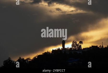 Chiang mai, Thaïlande. 18 octobre 2024. Les derniers rayons du soleil couchant disparaissent lentement au-dessus de l'horizon, avec le grand Bouddha debout en toile de fond à Wat Phra That Doi Kham. Les reflets du ciel au coucher du soleil affichent une variété de couleurs, telles que des teintes dorées et rouges, qui peuvent être vues chaque année en octobre avant l'arrivée de la saison d'hiver en Thaïlande. (Photo de Pongmanat Tasiri/SOPA images/Sipa USA) crédit : Sipa USA/Alamy Live News Banque D'Images