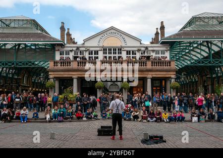 Artiste de rue avec foule de touristes devant l'entrée du marché Apple à Covent Garden. Londres, Angleterre. Banque D'Images