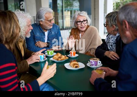 Femme grise plus âgée appréciant le café racontant quelque chose à un groupe d'amis assis ensemble à l'extérieur. Banque D'Images
