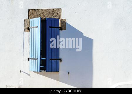 Vieille fenêtre avec volets en bois peints en bleu sur mur peint en blanc Banque D'Images