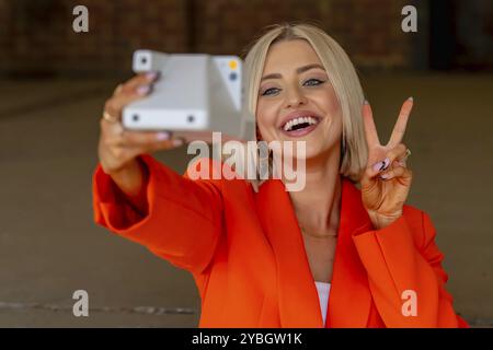 Un magnifique modèle blond pose à l'extérieur avec son appareil photo tout en profitant du temps printanier Banque D'Images