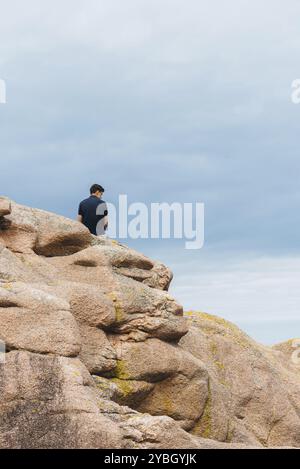 Jeune homme au sommet de formations rocheuses sur la Côte de granit rose autour de Perros-Guirec en Bretagne, France, Europe Banque D'Images