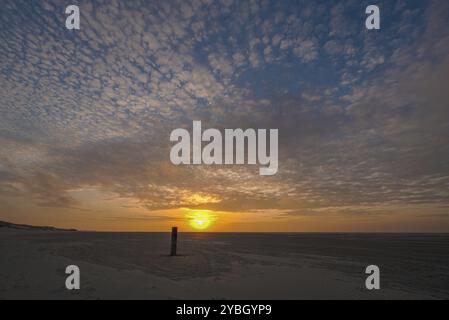 Coucher de soleil avec des couleurs orange vives contre un ciel avec des nuages blancs vus de la plage d'une île de Wadden dans le nord des pays-Bas Banque D'Images