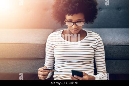 Femme noire, téléphone et carte de crédit pour le commerce électronique, le paiement ou l'achat dans le salon à la maison. Une femme africaine ou un cabas assis sur le sol avec Banque D'Images