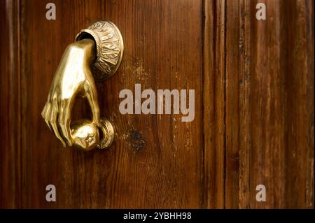 Gros plan d'un frappeur de porte en laiton orné en forme de main sur une porte en bois poli, soulignant l'élégance et le charme antique. Banque D'Images