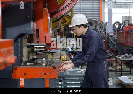 Un homme portant un casque et une combinaison de mécanicien combinaison de protection contre la poussière utilisant une machine pour façonner les pièces métalliques en toute sécurité. Atmosphère dans la manufacture avec grand machin Banque D'Images