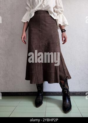 Tenue rétro, jupe en cuir de daim fin authentique Vintage, bottes cosaques de cowboy, Blouse bohème blanche, vue avant, Détails de la tenue, femme anonyme, Brown A Line Boho Patchwork jupe midi, jupe café Banque D'Images