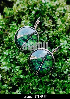 Boucles d'oreilles en résine faites à la main de vraies feuilles vertes enveloppées dans une finition transparente à fond de mousse verte fermer. Crochets Leverback, bijoux inspirés de la nature Banque D'Images
