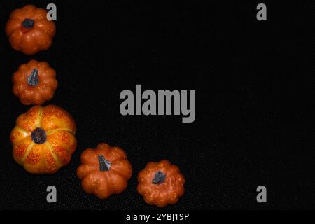 Vue de dessus sur citrouilles oranges artificielles sur le côté gauche d'un fond noir avec espace de copie, cadre d'automne Banque D'Images