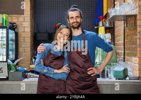 Embrasser un couple de collègues partenaires jeunes homme et femme dans des tabliers sur le lieu de travail Banque D'Images