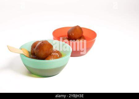 Deux bols remplis de délicieux dessert indien Gulab Jamun dans des bols rouges et verts sur fond blanc. Banque D'Images