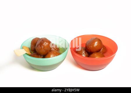 Deux bols remplis de délicieux dessert indien Gulab Jamun dans des bols rouges et verts sur fond blanc. Banque D'Images
