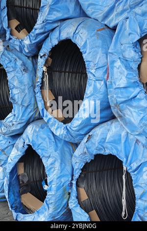 Rouleaux empilés de treillis métallique noir enveloppés dans du carton, placés sur une bâche bleue. Banque D'Images