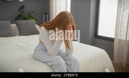 Une jeune femme en détresse est assise se couvrant le visage avec les mains sur un lit dans une chambre, suggérant l'inquiétude ou la tristesse dans un cadre familial. Banque D'Images