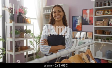 Jeune femme debout avec les bras croisés dans un magasin de décoration entourée de décorations intérieures, de plantes et d'œuvres d'art. Banque D'Images