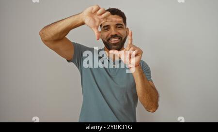 Beau jeune homme hispanique faisant un geste de cadre avec ses mains tout en souriant sur un fond blanc isolé Banque D'Images