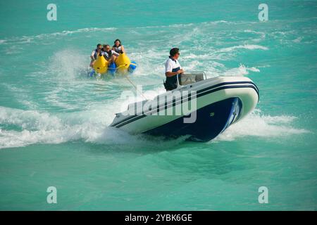 Les gens s'amusant sur un bateau de banane gonflable étant remorqué à grande vitesse derrière une côte. Banque D'Images