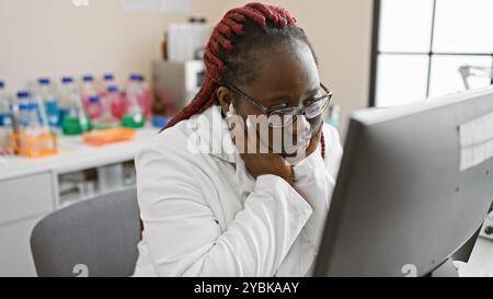 Une femme afro-américaine concentrée avec des tresses travaillant dans un laboratoire devant un ordinateur Banque D'Images