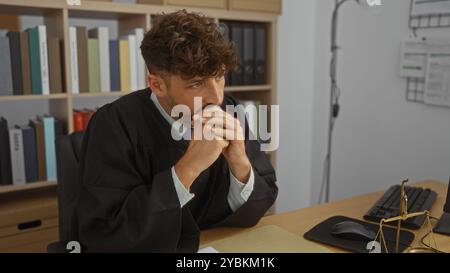 Jeune homme dans la robe d'un juge regardant contemplatif à son bureau dans un cadre professionnel de travail Banque D'Images