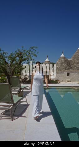 Une belle jeune femme hispanique profitant d'une journée ensoleillée au bord d'une piscine à alberobello, en italie, entourée de maisons traditionnelles de trulli. Banque D'Images