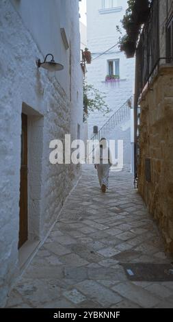 Une jeune femme se promène dans une rue étroite et pittoresque à polignano a mare, pouilles, italie, entourée de bâtiments en pierre blanche et de détails charmants. Banque D'Images