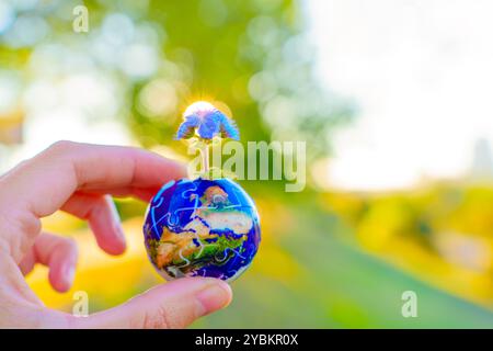 Main tenant une pièce de puzzle en forme de globe avec une fleur qui pousse de lui, symbolisant la Terre et la préservation de la vie. Banque D'Images