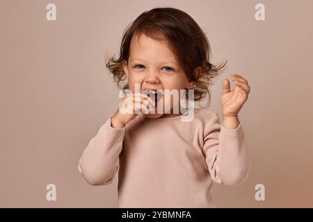 fille enfant positive mignonne mangeant pastille de fruits sur fond beige. alimentation saine pour bébé. Banque D'Images