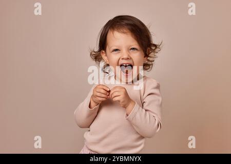 souriante fille enfant très excitée tenant pastille de fruits sur fond beige. alimentation saine pour bébé. Banque D'Images