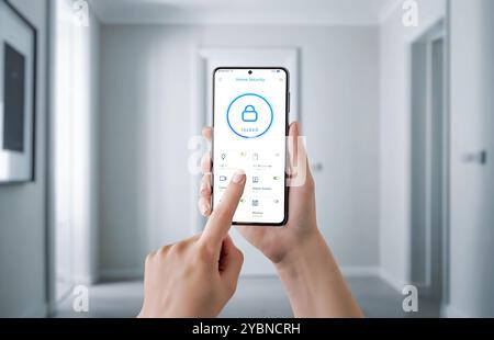 Main tenant un smartphone avec une interface d'application de sécurité, contrôlant les fonctions de sécurité de la maison comme la serrure de porte, la caméra de surveillance et les alarmes. Concept de Banque D'Images