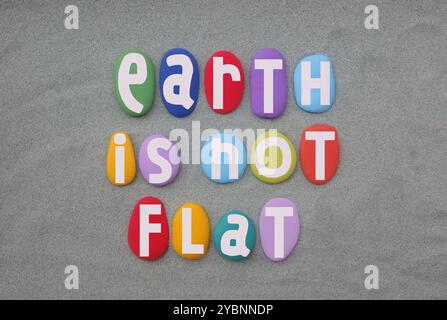 Earth is not plat, slogan créatif composé de lettres en pierre multicolores peintes à la main sur du sable vert Banque D'Images