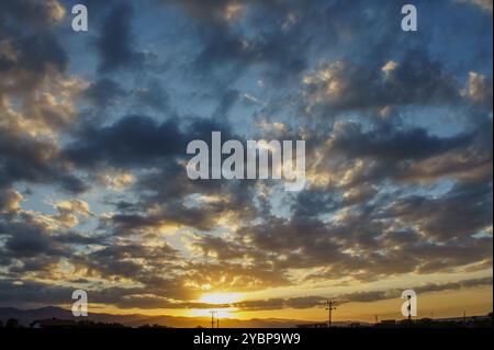 Le soleil plonge sous l'horizon, projetant une lueur chaude à travers le ciel, où les nuages moelleux se rassemblent dans une gamme étonnante de couleurs, créant une soirée sereine Banque D'Images