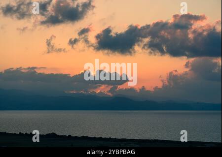 Le ciel se transforme à l'approche du crépuscule, mettant en valeur un brillant affichage de couleurs où le soleil plonge sous l'horizon, projetant des reflets sur la wa sereine Banque D'Images