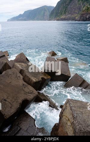 Blocs brise-lames en béton le long de la côte de Seixal avec en toile de fond des falaises luxuriantes et le vaste océan Atlantique Banque D'Images