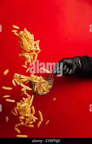 Photo dynamique de frites volantes tombant d'un panier sur fond rouge vif Banque D'Images