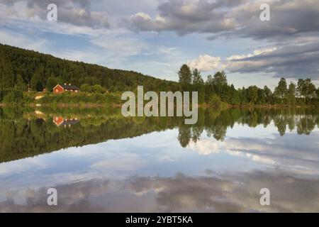 Belle soirée au-dessus de la rivière Klaralven près de Branas avec une maison en bois fautée se reflétant dans l'eau Banque D'Images