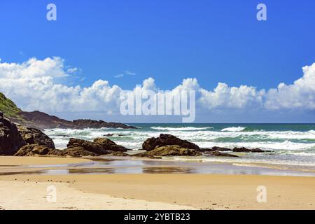 Plage avec des vagues se brisant contre les rochers par une journée ensoleillée dans la ville de Serra Grande sur la côte de Bahia Banque D'Images