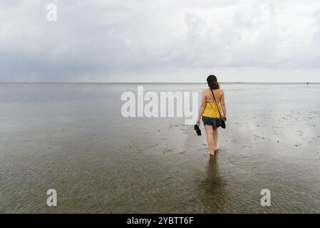 Jeune femme marchant seule sur une plage calme et tranquille à marée basse dans la mer de Wadden, en Allemagne. Vue de derrière Banque D'Images