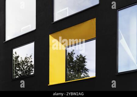 Fenêtre jaune sur façade noire avec reflet de l'arbre vert. Arrière-plan de l'architecture abstraite Banque D'Images