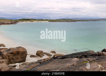 Soirée à Gurteen Bay, Irlande, capture le littoral paisible avec ses eaux turquoises claires et ses formations rocheuses. Le sable blanc doux rencontre le s. Banque D'Images