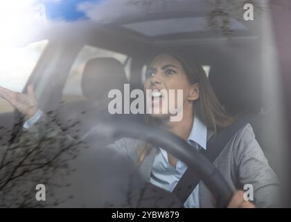 Femme d'affaires bouleversée conduisant la voiture et criant sur les autres conducteurs dans la circulation Banque D'Images