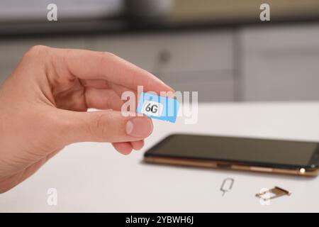 Femme avec carte SIM 6G à la table blanche à l'intérieur, gros plan Banque D'Images