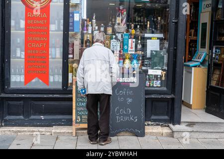 Réflexions du temps : un homme âgé observant la vitrine d'un magasin d'alcool local Banque D'Images