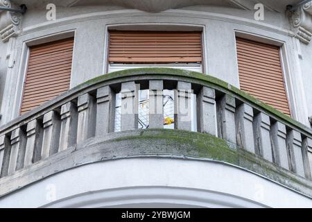 Vieux balcon incurvé avec piliers de clôture en béton et cadres de fenêtre avec stores bruns. Banque D'Images