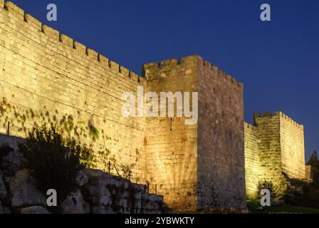 Une section des anciens remparts et murs de pierre de la vieille ville de Jérusalem, illuminée par la lumière artificielle au crépuscule en Israël. Banque D'Images