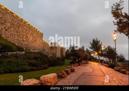 Une section des anciens remparts en pierre et des murs de la vieille ville de Jérusalem et la route adjacente, éclairée par des lumières décoratives sur le mont. Zion. Banque D'Images