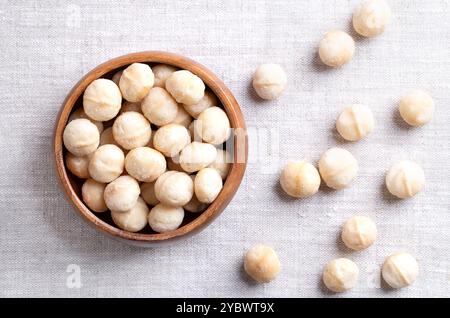 Noix de macadamia, rôties et salées, dans un bol en bois sur tissu de lin. Également connu sous le nom de noix du Queensland, noix de brousse, noix maroochi, bauple et noix d'Hawaï. Banque D'Images