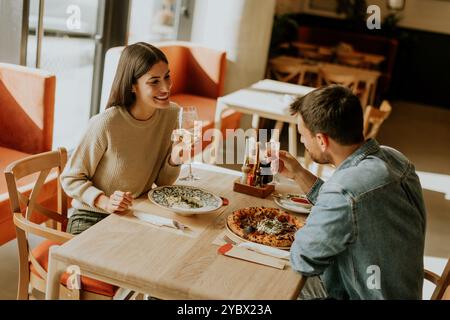 Deux personnes savourent leurs boissons à une table en bois, immergées dans une ambiance de restaurant détendue, tout en étant profondément dans la conversation et les rires. Banque D'Images