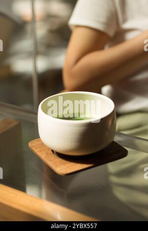 Dans un cadre tranquille, un bol en céramique rempli de matcha vert vif se trouve sur un dessous de verre en bois, capturant l'essence du calme et de la tradition. Banque D'Images